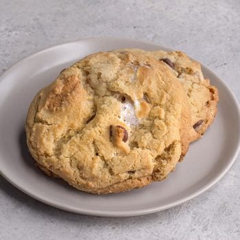 Two large, golden-brown chocolate chip cookies sit on a round, light gray plate against a light gray textured background.